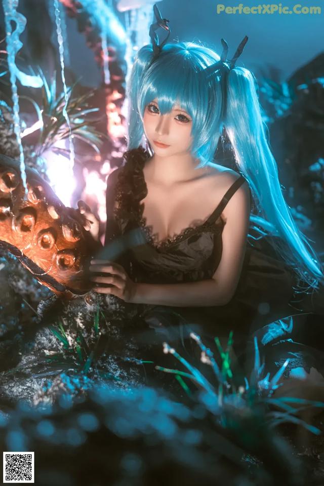 A woman with long blue hair sitting on a rock.