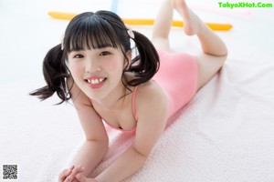 A little girl in a pink bathing suit laying on a pink towel.