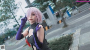 A woman in a black and purple outfit leaning against a wall.