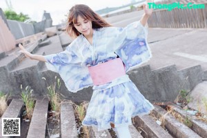 A woman in a blue and white kimono holding a green leaf.