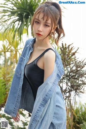 A woman in a denim shirt and black shorts posing by a window.