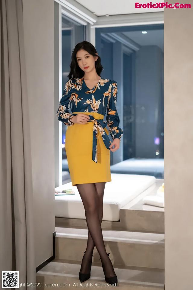 A woman in a yellow skirt and a blue blouse posing for a picture.