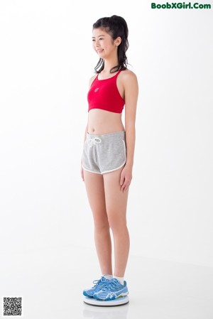A woman in a red sports bra top and gray shorts standing on a scale.