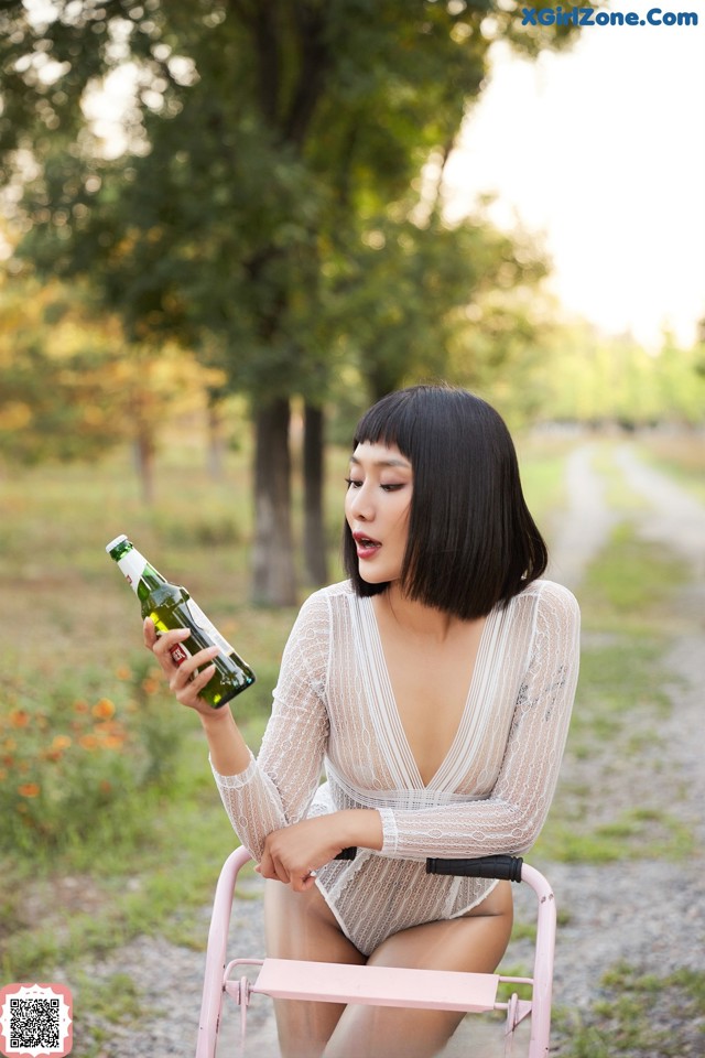 A woman sitting on a pink chair holding a bottle of beer.