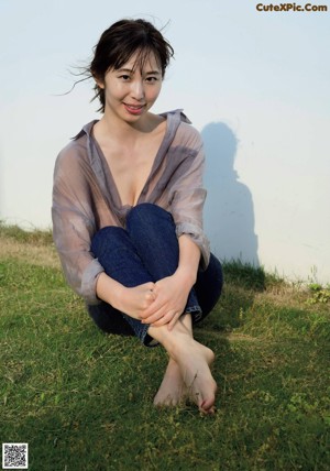 A woman sitting on the grass with her legs crossed.