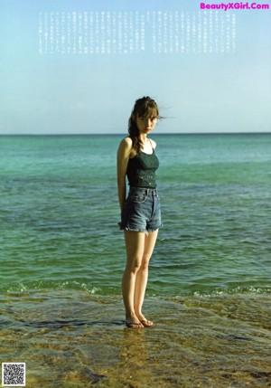 A woman in a green bikini sitting on the sand.