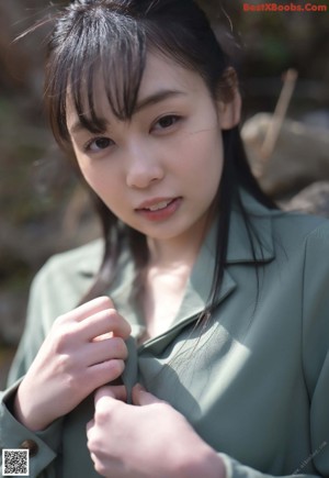 A woman in a green shirt and white panties leaning against a fence.