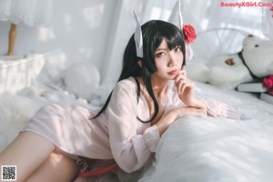 A woman in a pink robe sitting on a bed with flowers.