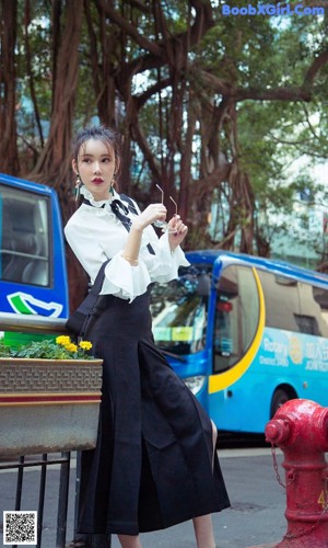 A woman sitting on a fire hydrant in front of a bus.