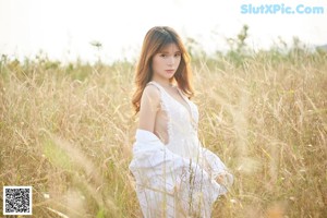 A woman in a white dress sitting in a field of tall grass.