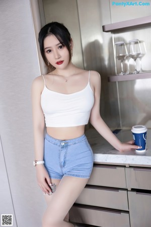 A woman in a white top and blue shorts standing in a kitchen.