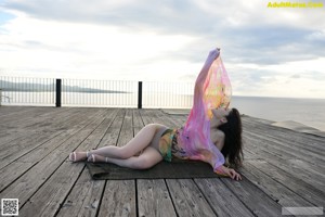 A naked woman standing on a wooden dock holding a scarf.