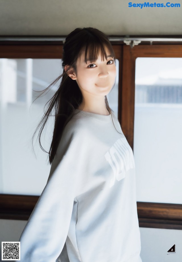 A woman standing in front of a window wearing a white sweatshirt.