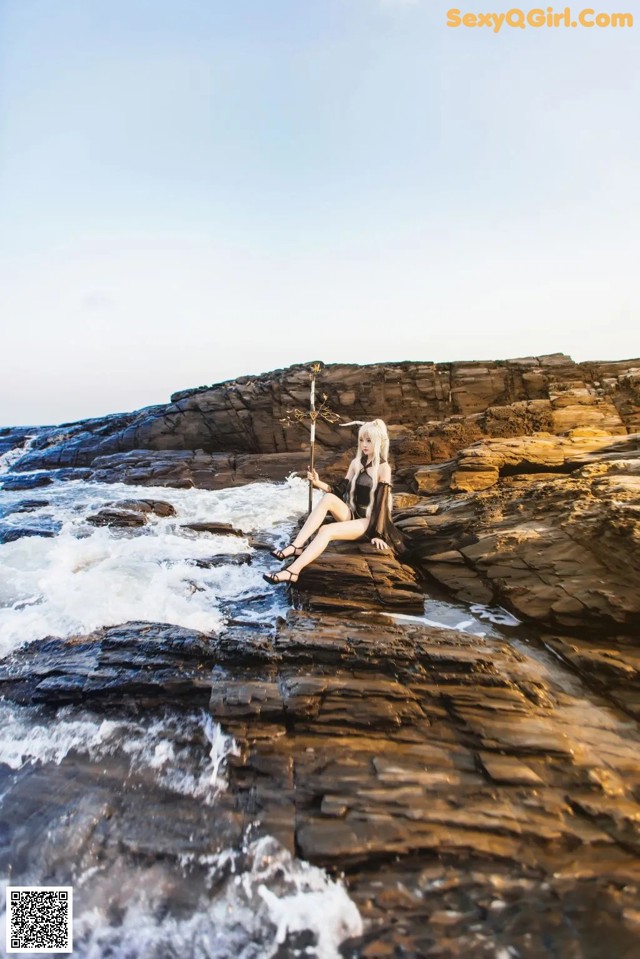 A woman sitting on a rock by the ocean.