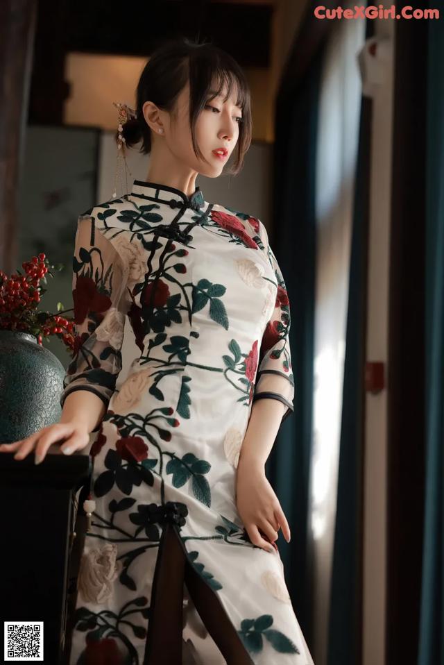 A woman in a white and red cheongsam sitting on a chair.