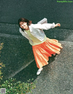 A woman in a beige jacket is looking up at the sky.