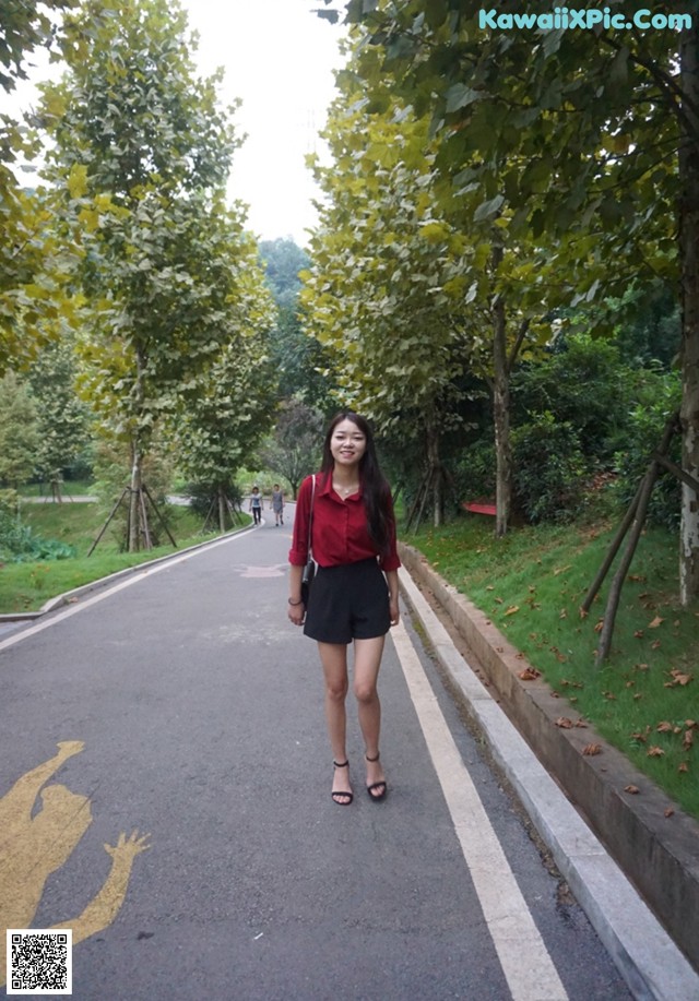 A woman in a red shirt and black shorts standing on a road.