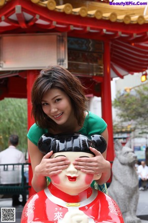 A woman taking a picture of a red archway with chinese writing.